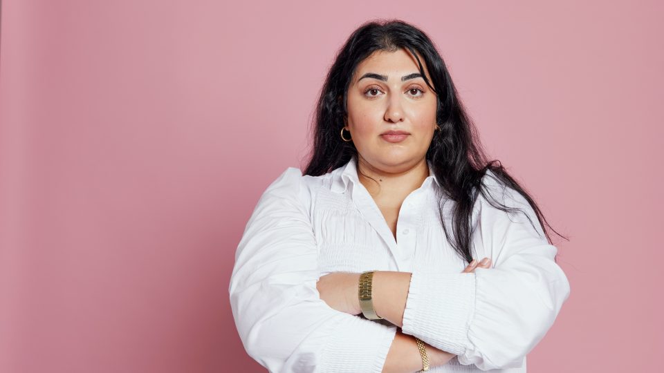 Roks ordförande Adine Samadi med armarna i kors mot rosa bakgrund.